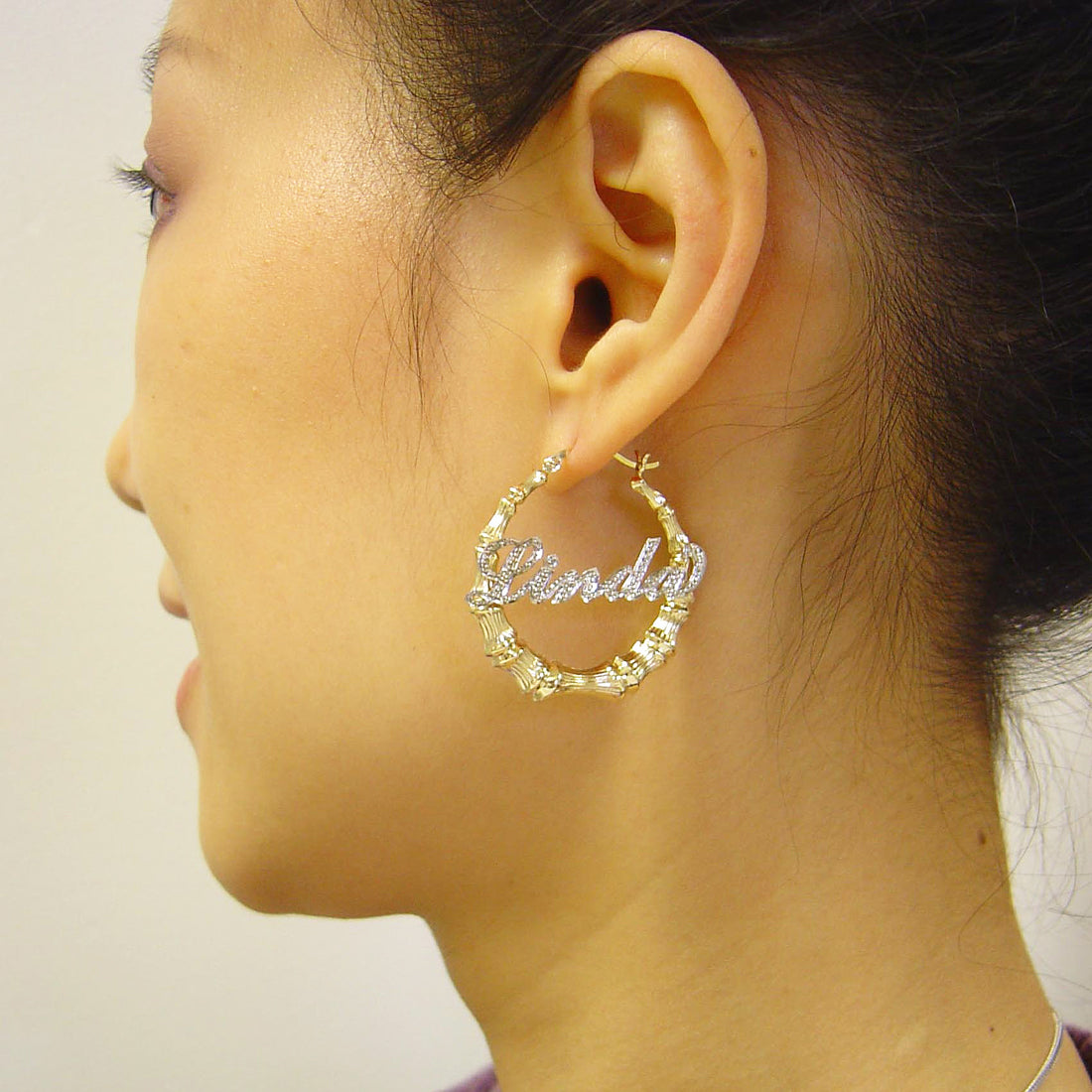 Model wearing 1.3-inch personalized two-tone gold iced out bamboo name hoop earrings