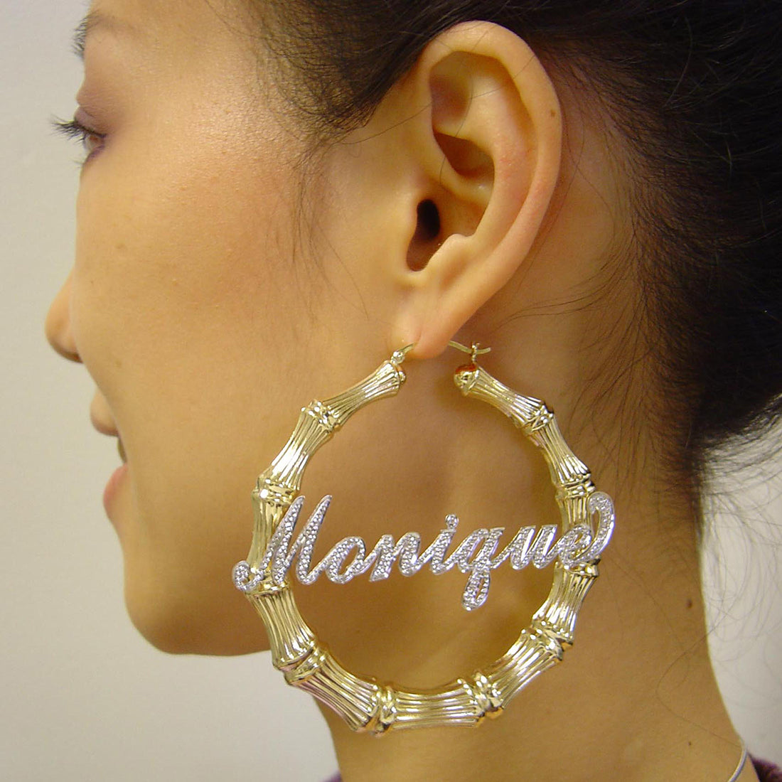 Model wearing 2.9 inch large custom two-tone gold bamboo name hoop earrings with iced-out accents