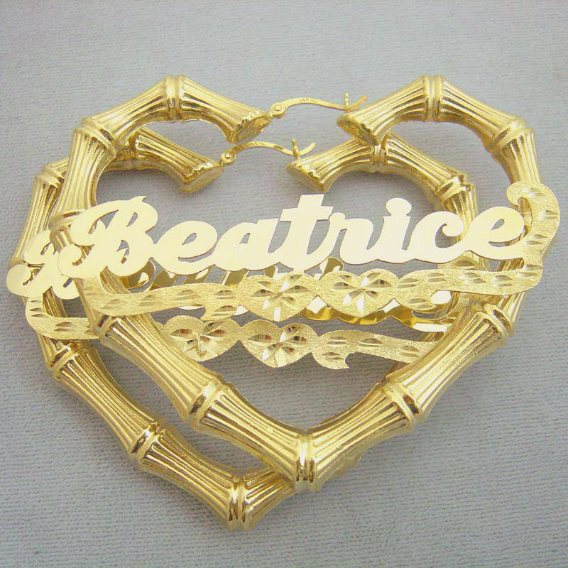 A pair of gold heart-shaped bamboo hoop earrings with the name 'Beatrice' written in cursive script and decorated with diamond-cut underlining, displayed against a neutral background.