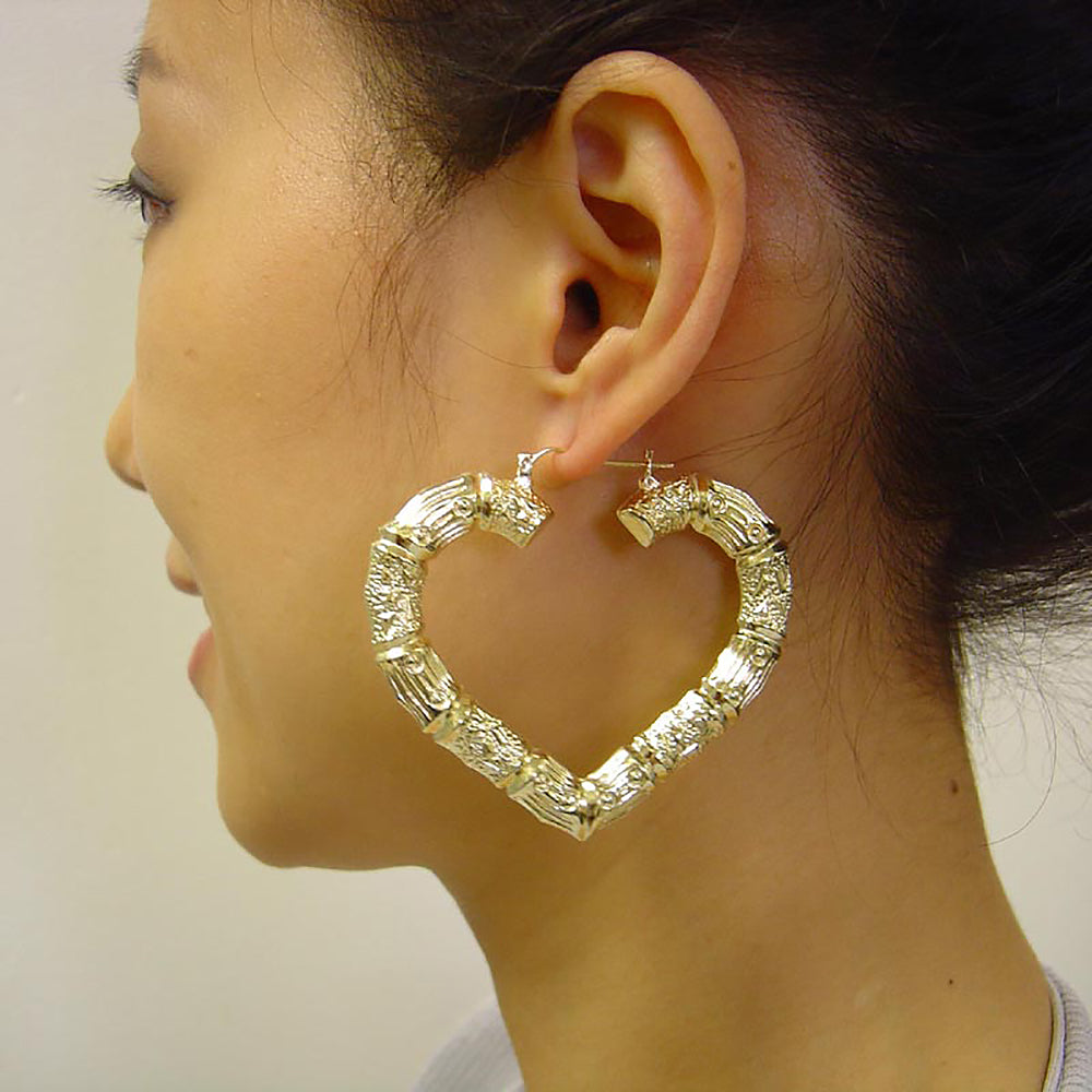 Woman wearing 2.5 inch 10K yellow gold puffed heart bamboo hoop earrings