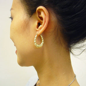 Model wearing small 10K gold oval bamboo doorknocker hoop earrings