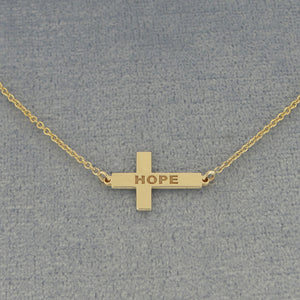 A gold cross pendant necklace engraved with the word 'HOPE'