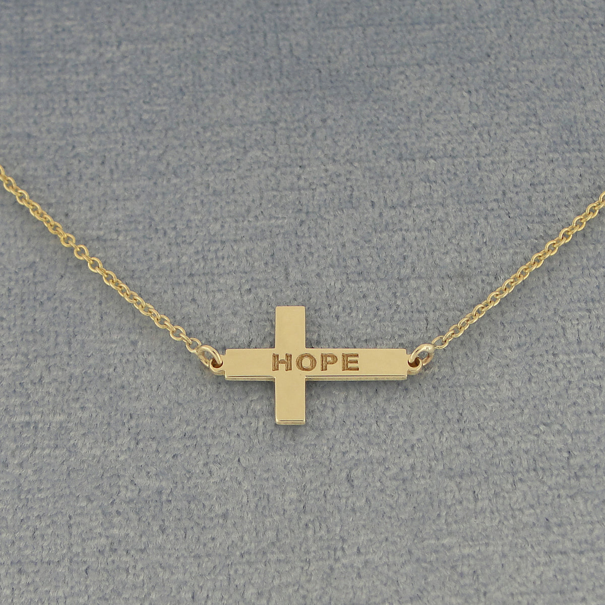 A gold cross pendant necklace engraved with the word 'HOPE'