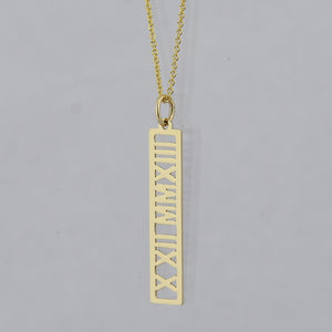 A gold necklace featuring a vertical rectangular pendant with Roman numerals cut out