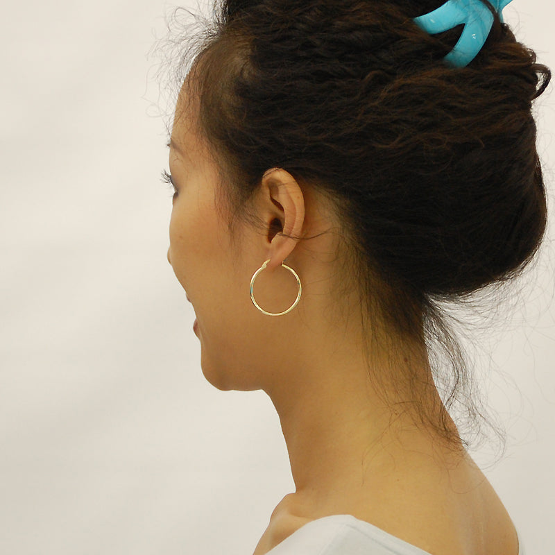 Model wearing 30mm 14K yellow gold 2mm hollow hoop earrings showing size and fit