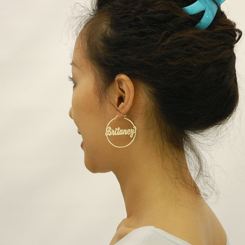 Model wearing custom 14k yellow gold name hoop earrings 40mm diameter