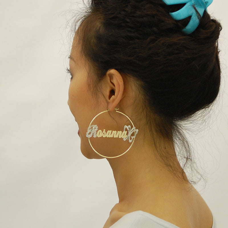Close-up of custom nameplate with iced-out initial letter and butterfly endpoint on 14k gold hoop earring