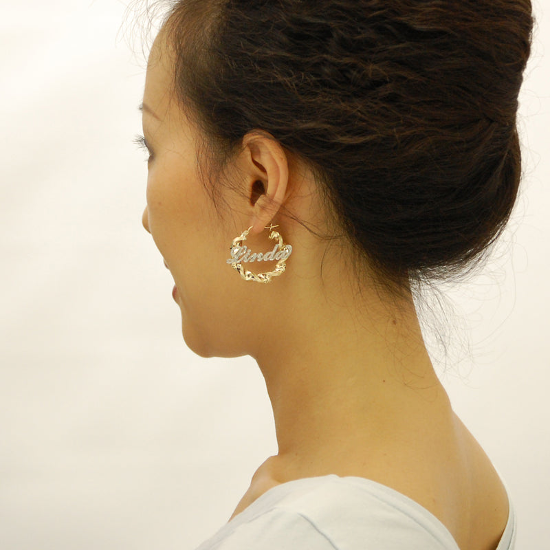 Woman wearing 1.6-inch personalized 10k gold iced out twisted name hoop earrings.