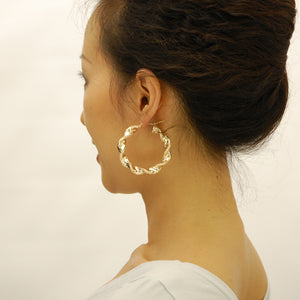 Model wearing 2-inch wide 10K yellow gold 8mm thick twisted hoop earrings