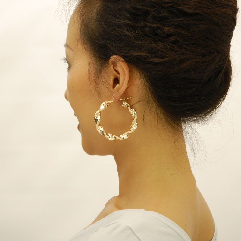 Model wearing 2-inch wide 10K yellow gold 8mm thick twisted hoop earrings