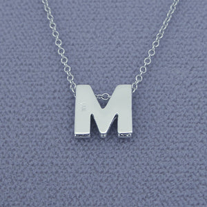 Solid gold 3D double plate diamond initial pendant styled flat on gray background
