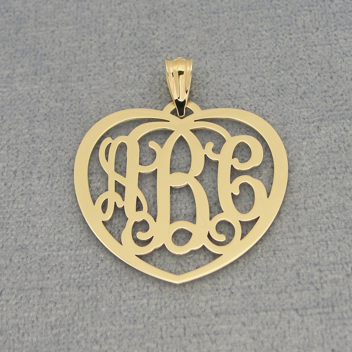 Flat lay of personalized solid gold heart monogram pendant with three initials on gray background