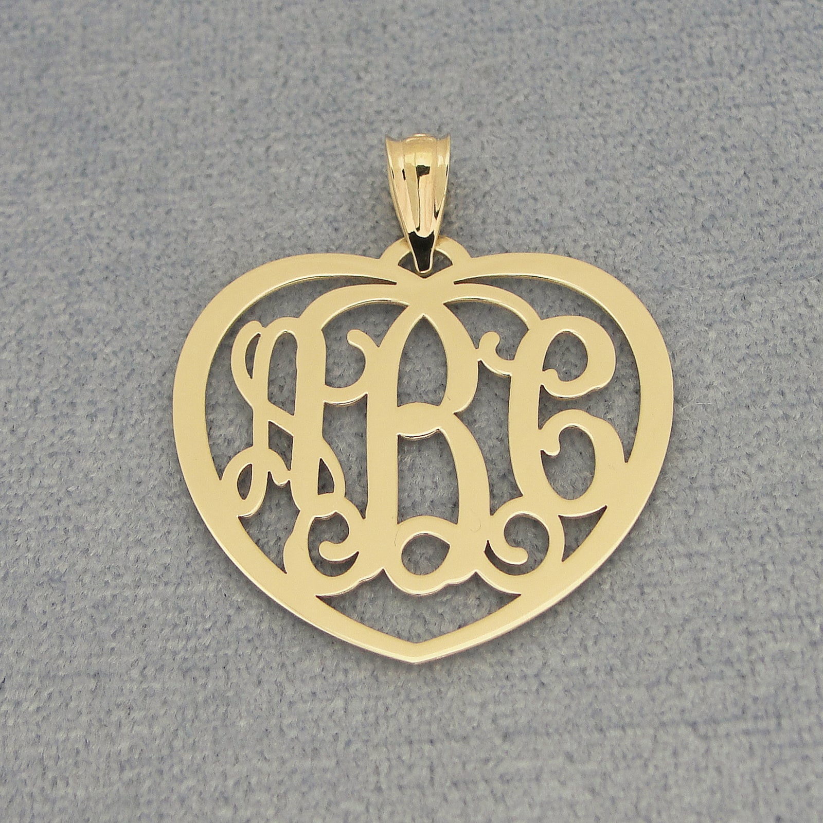 Flat lay of personalized solid gold heart monogram pendant with three initials on gray background