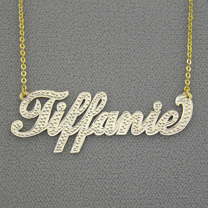 Close-up view of personalized gold script nameplate pendant showing diamond-cut rhodium finish and solid gold stamp