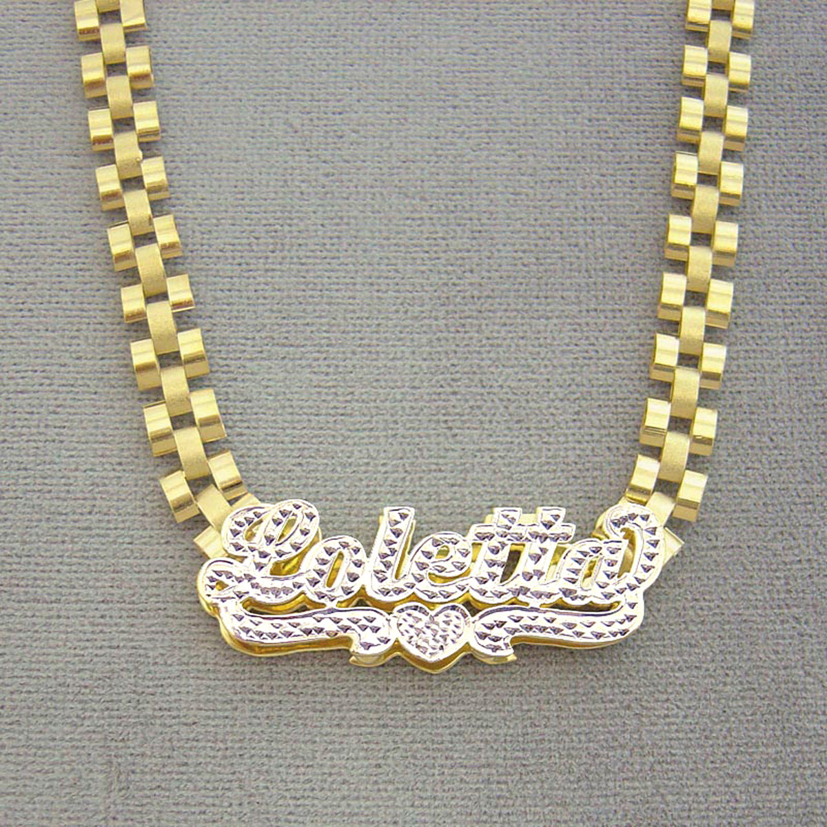 Custom 10K yellow gold iced out nameplate laying flat on 6mm watch-band style chain
