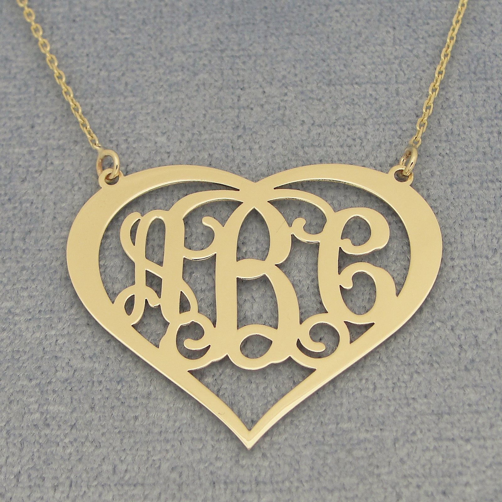 Close-up of a custom 14k gold heart monogram pendant with three personalized initials.