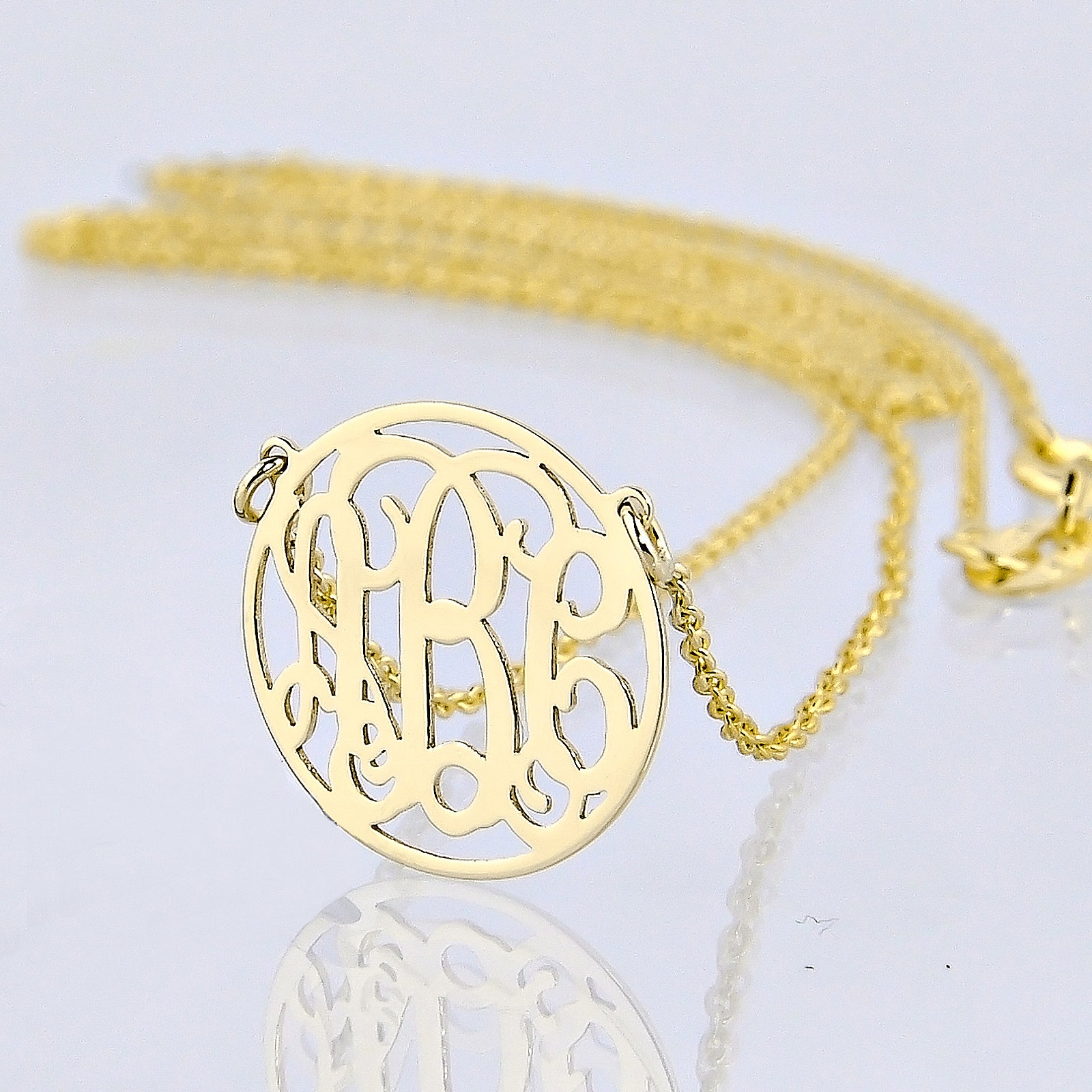 Close-up of an extra small personalized solid gold three-initial circle monogram necklace with reflection.
