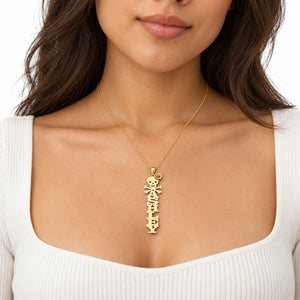 Model wearing an Ashley gold vertical name necklace with skull and crossbones and a rose accent, shown with a white scoop-neck top.