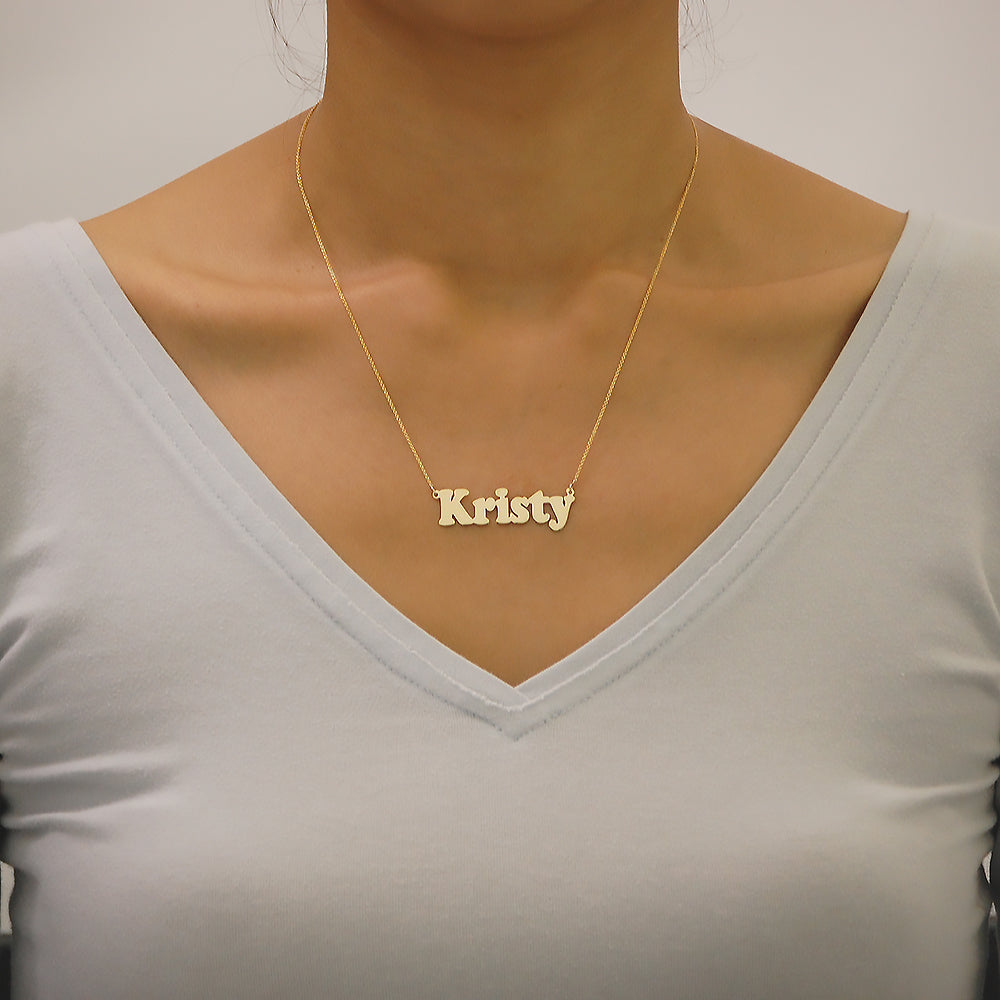Model wearing a personalized solid gold bold block letter nameplate necklace.
