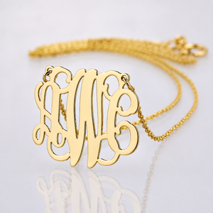 Small solid yellow gold three-initial monogram pendant with chain on reflective white surface