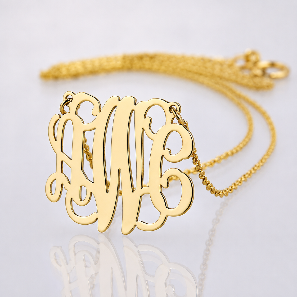 Small solid yellow gold three-initial monogram pendant with chain on reflective white surface