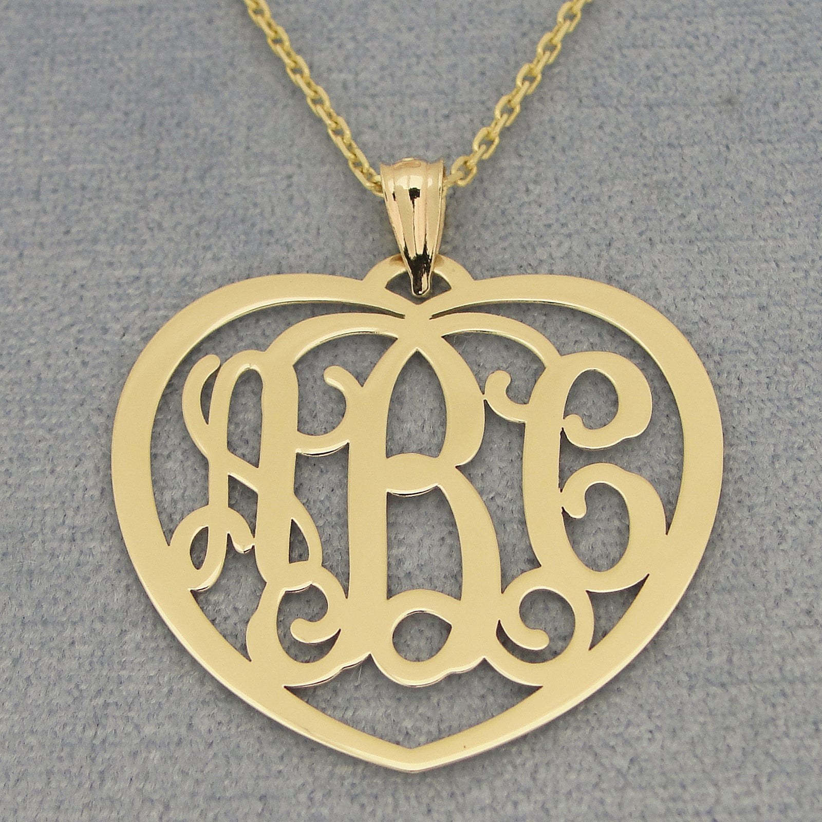 Yellow gold 3-initial heart monogram pendant necklace on a textured gray background.