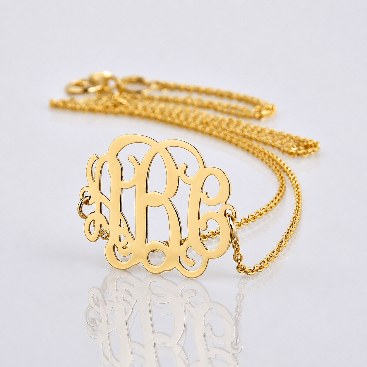 Close-up of a solid 14k yellow gold three-initial sideways monogram necklace with a soft reflection