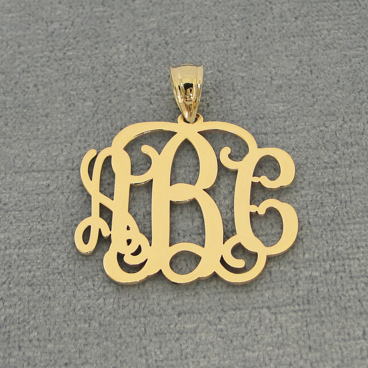 Solid yellow gold three-initial custom monogram pendant displayed against a gray jewelry background.