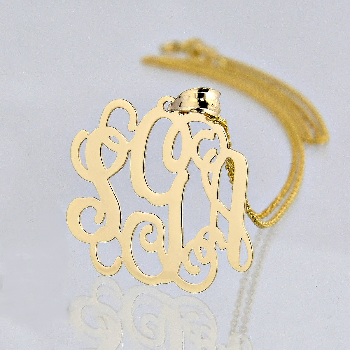 Close-up of a solid yellow gold three-initial monogram pendant on a fine chain with reflection.