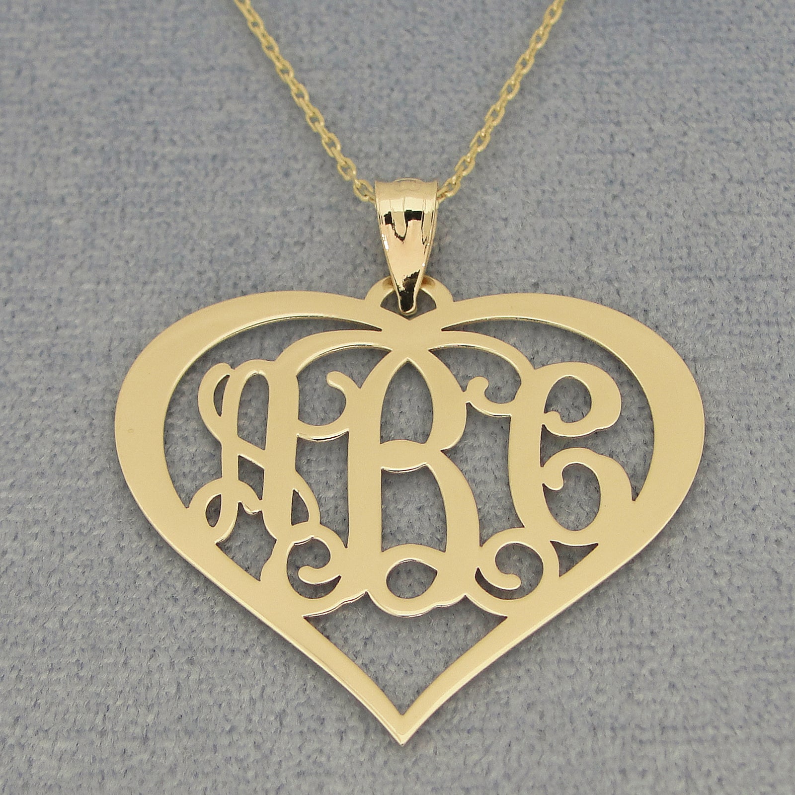 Detail view of a custom yellow gold 3-initial heart monogram pendant on chain
