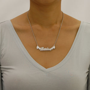 Model wearing a personalized sterling silver 3D nameplate necklace with heart motifs and an 18-inch Rolo chain.