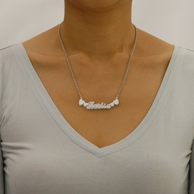 Model wearing a personalized sterling silver 3D nameplate necklace with heart motifs and an 18-inch Rolo chain.