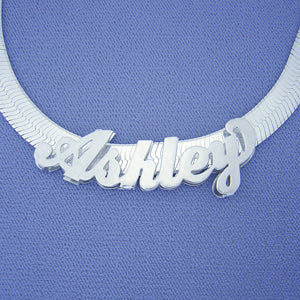 Close-up view of a custom 3D curved name necklace spelling "Monique" on a wide sterling silver herringbone chain.