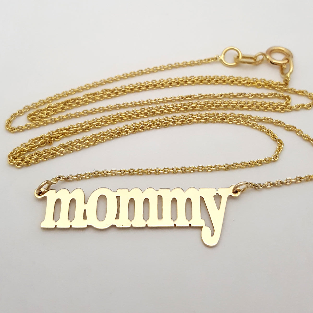 Comparison of 10k and 14k solid gold mommy script nameplate necklaces stacked together.