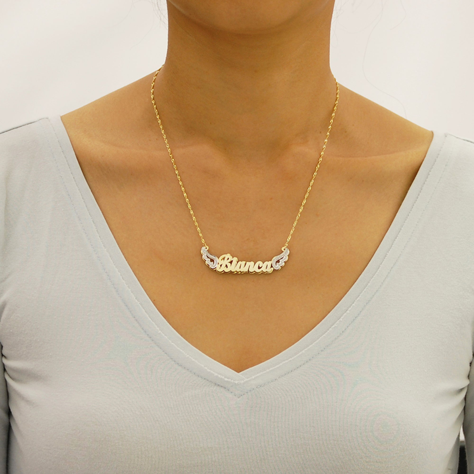 Model wearing personalized 14k gold angel wings 3D nameplate necklace.