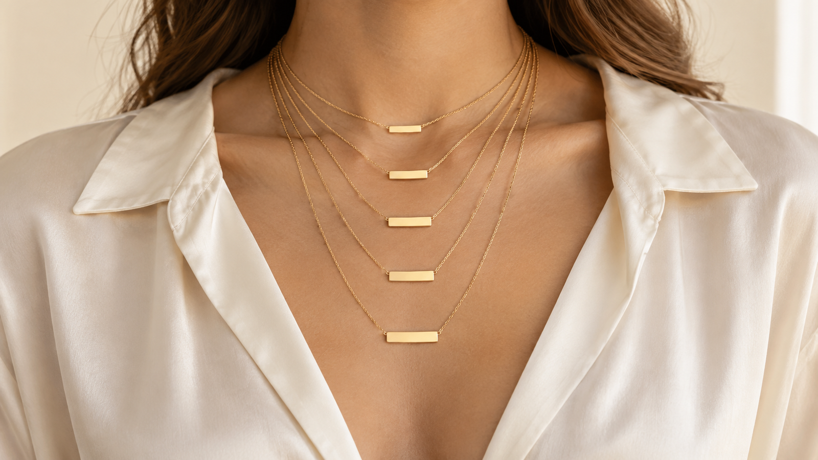 Layered gold nameplate necklaces showing 14 to 24 inch chain lengths on an ivory blouse