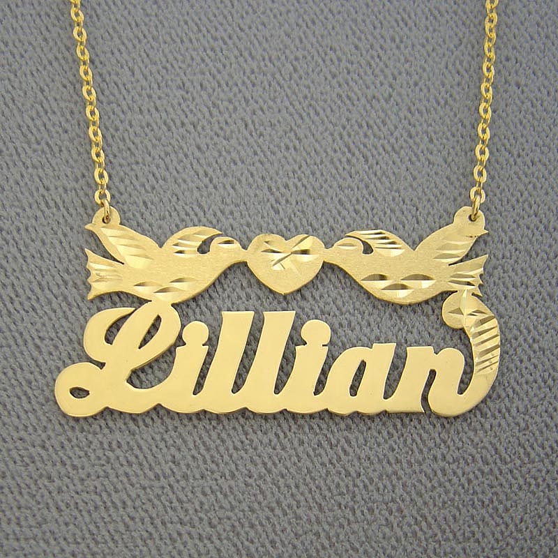 Close-up display of a custom gold nameplate necklace with diamond-cut heart accents and a two-birds design rendered in elegant script lettering.