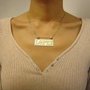 Model wearing a personalized solid gold rectangular name pendant on a yellow gold chain.