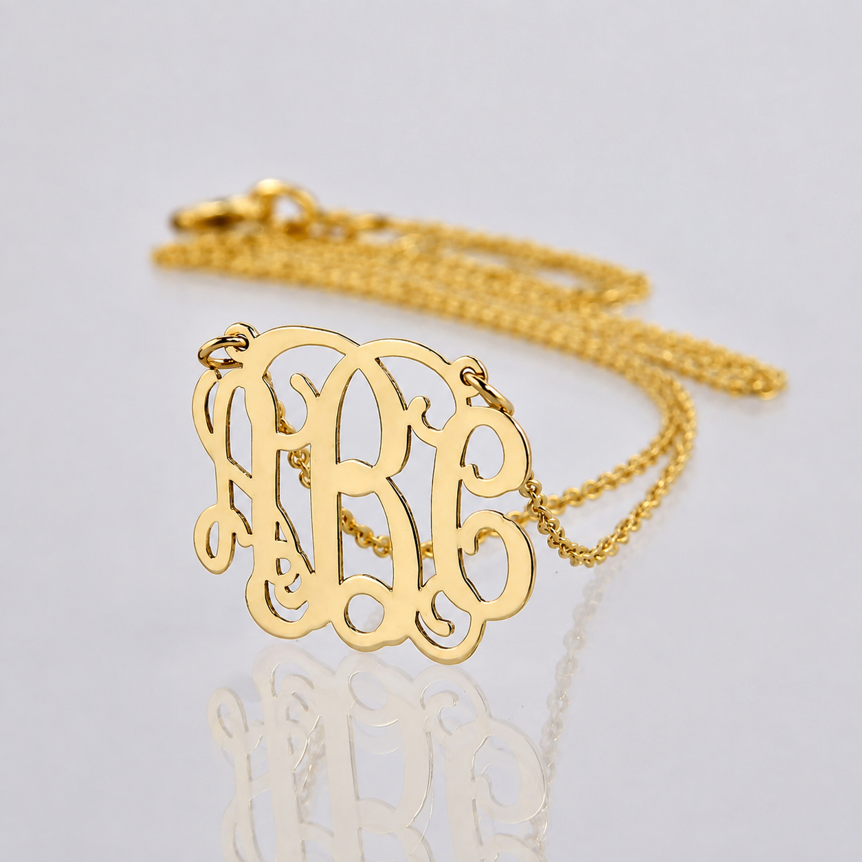 Angled detail view of personalized mini 3-initial monogram necklace showing 14k yellow gold thickness and polish