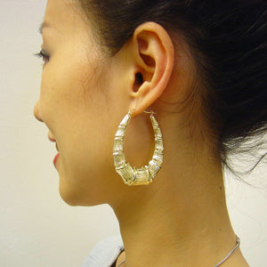 Model wearing 1.5 inch wide 10K gold drop down oval bamboo hoop earrings