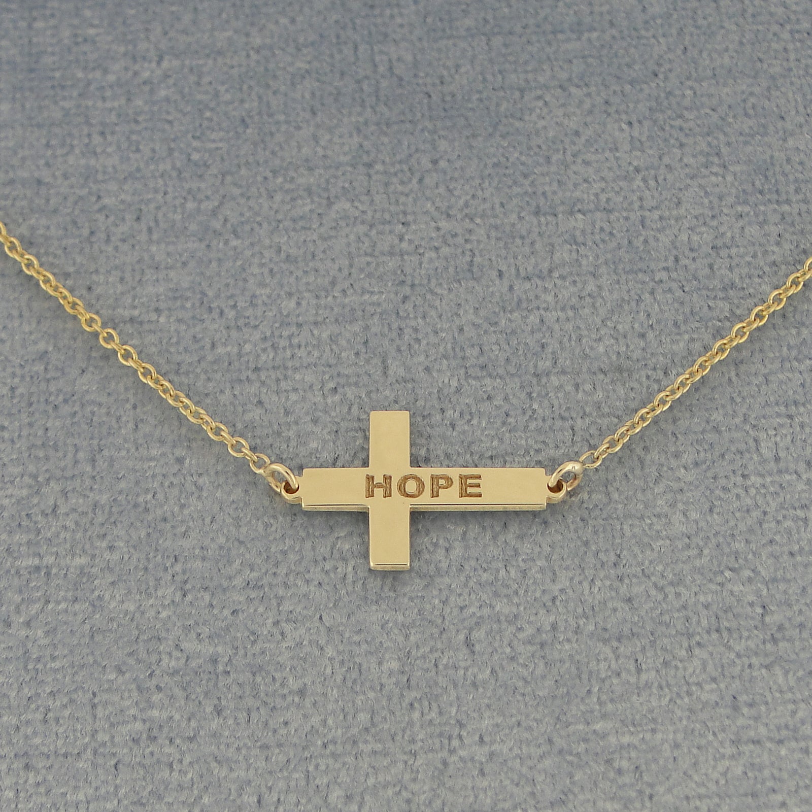A gold cross pendant necklace engraved with the word 'HOPE' 