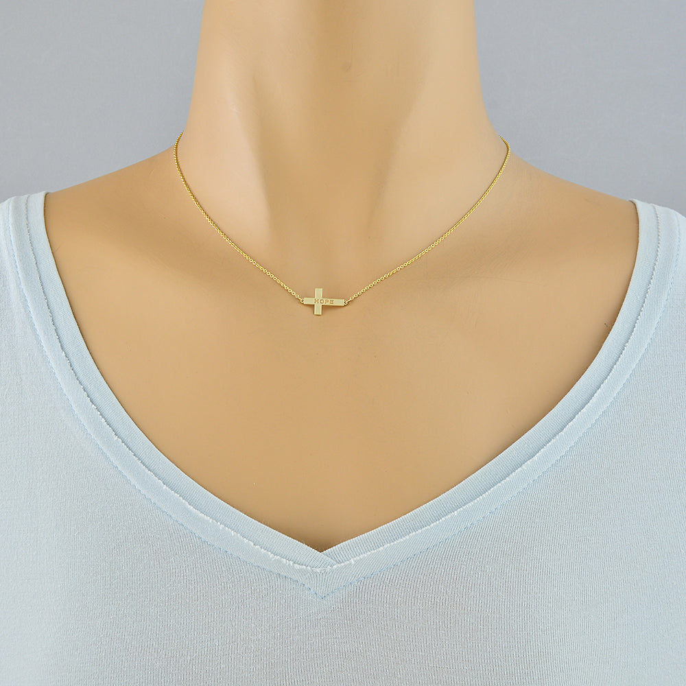 A delicate gold cross pendant necklace displayed on a mannequin