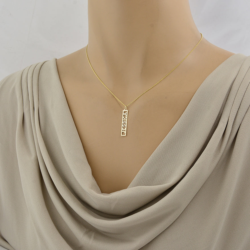 A gold necklace with a vertical rectangular pendant on a mannequin.