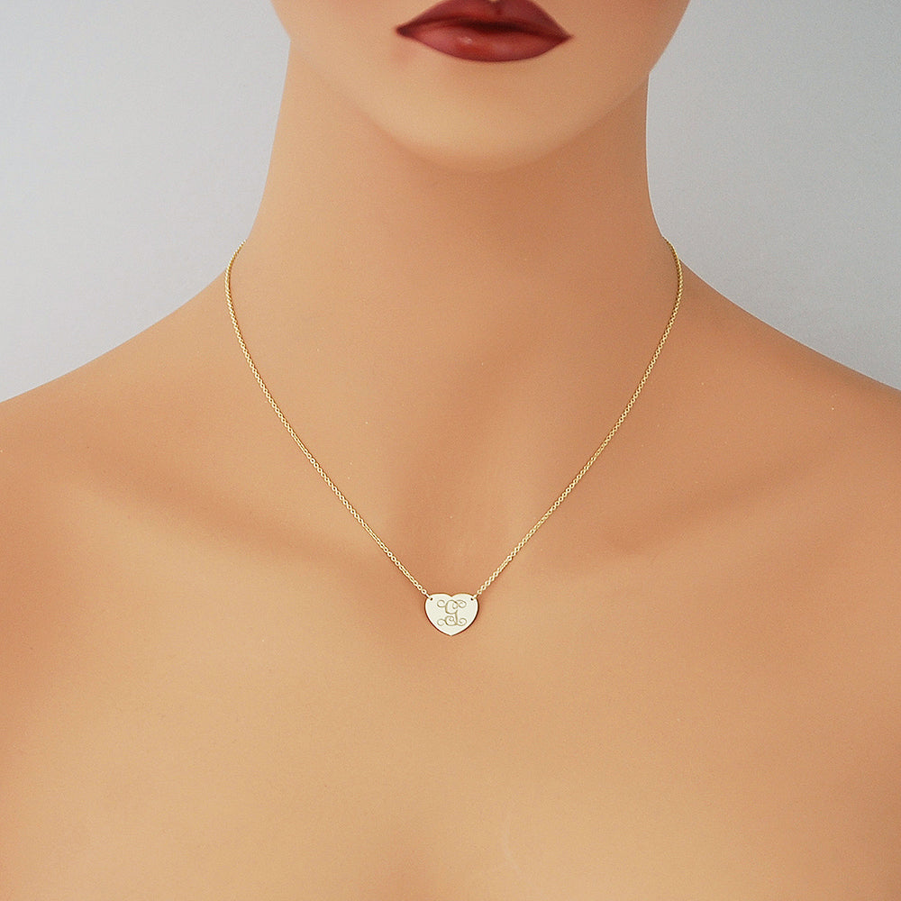 A delicate gold chain necklace with a small heart-shaped pendant engraved with monogram initial displayed on a mannequin.