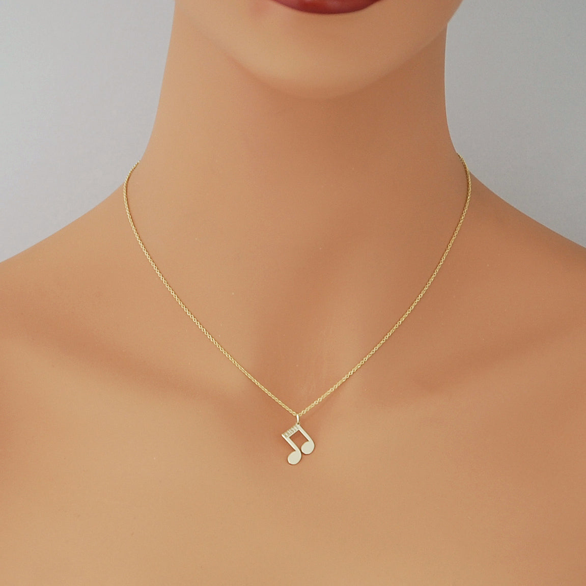 A delicate gold chain necklace with a small musical note pendant displayed on a mannequin
