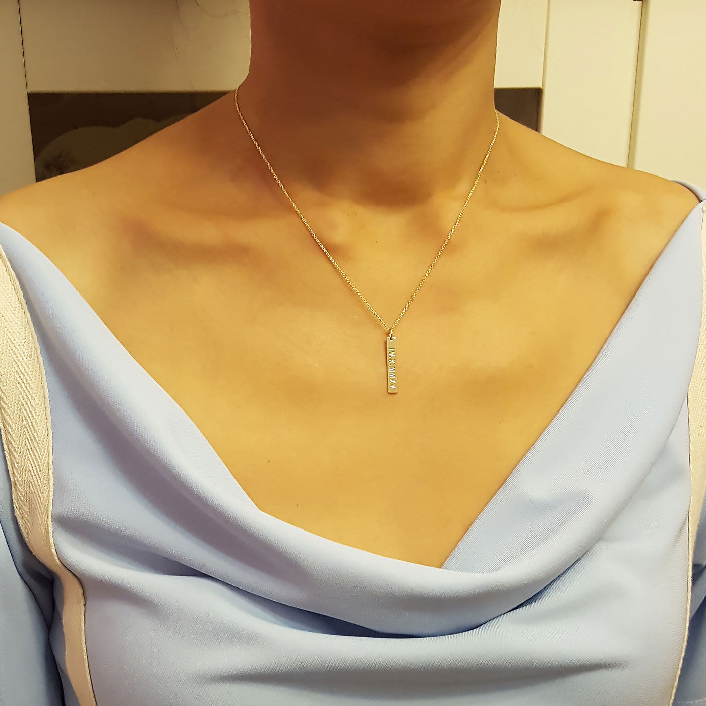 Woman wearing dainty personalized 14k yellow gold vertical bar necklace on fine rolo chain