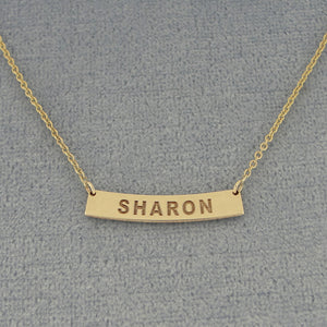 A gold bar necklace with the name 'SHARON' engraved on a curved horizontal bar.