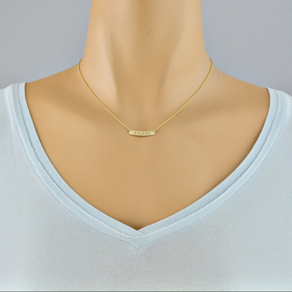 Mini custom engraved solid gold name bar necklace styled on a model for layering