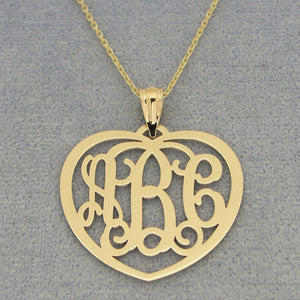 Close-up of custom solid gold heart monogram pendant with three initials on a gold chain and gray background