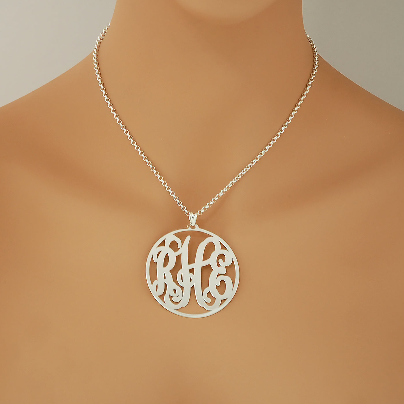 Woman wearing a 2-inch sterling silver circle monogram pendant necklace on a silver chain over a neutral outfit.